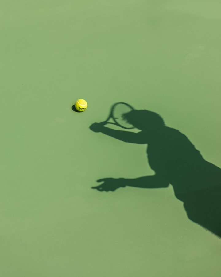 A player casting a long shadow on a green court